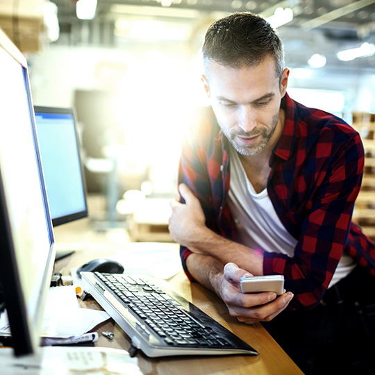man using a smartphone while sat in front of a computer